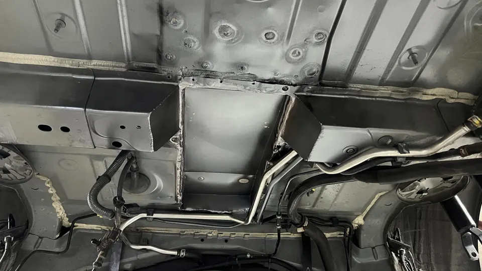 Undercarriage view of a performance car showing chassis, custom fabrication, and various lines in a shop environment.