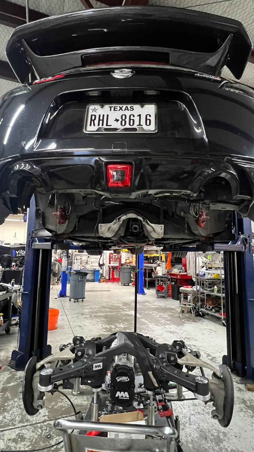 A black Nissan 370Z on a lift in a shop with its rear subframe and suspension removed for service or upgrade.