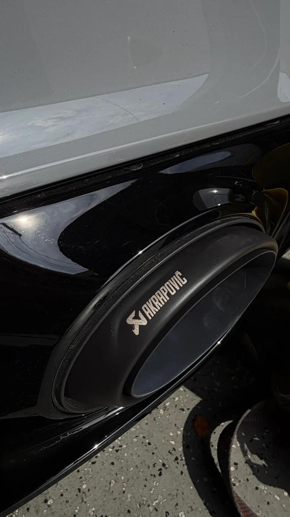 Close-up of a black Akrapovic exhaust tip on a car's rear bumper.