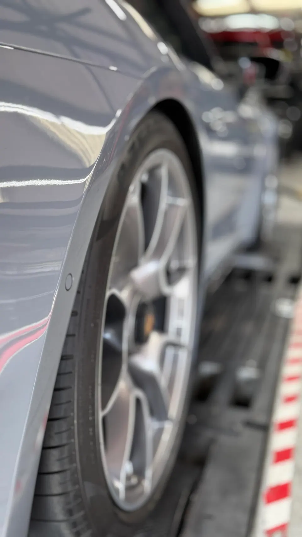 Close-up of a grey Porsche's rear wheel and fender, highlighting the multi-spoke wheel and tire in a shop setting.