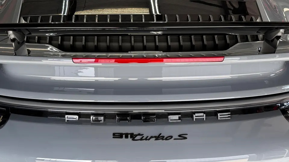 Rear view of a grey Porsche 911 Turbo S, showcasing the engine cover, active spoiler, and model badging.