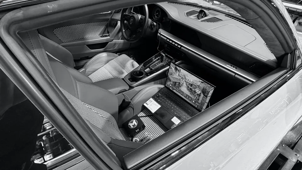 Interior view of a Porsche with a laptop on the passenger seat, showcasing the center console and houndstooth pattern.