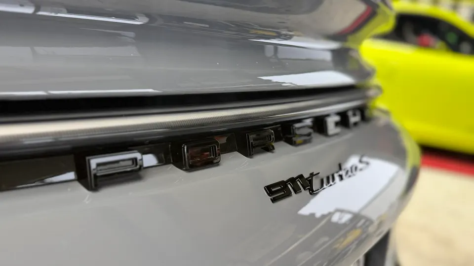 Close-up of the PORSCHE 911 Turbo S emblem on the rear of a grey Porsche sports car.