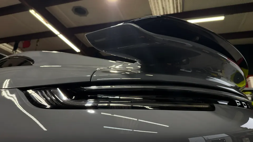 A close-up of the rear of a grey Porsche, highlighting the black rear wing and LED taillight.