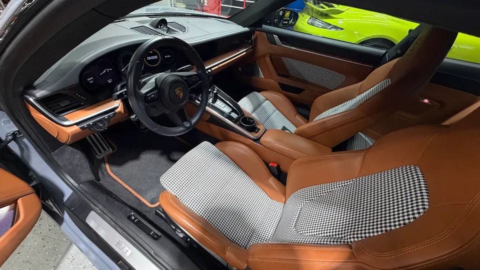 Detailed view of a Porsche interior featuring brown leather seats with houndstooth inserts, steering wheel, and dashboard.