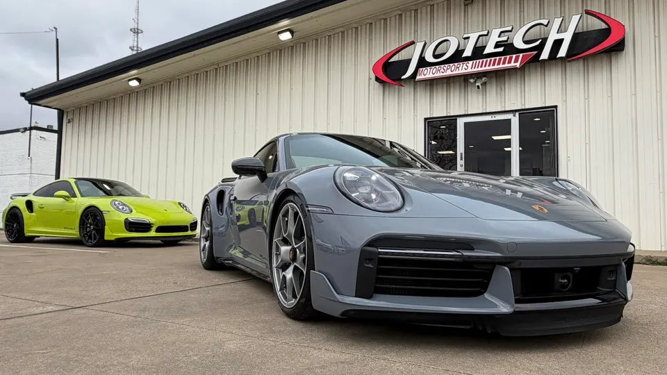 Two Porsche 911 Turbo S cars, one grey and one lime green, parked outside Jotech Motorsports performance shop.