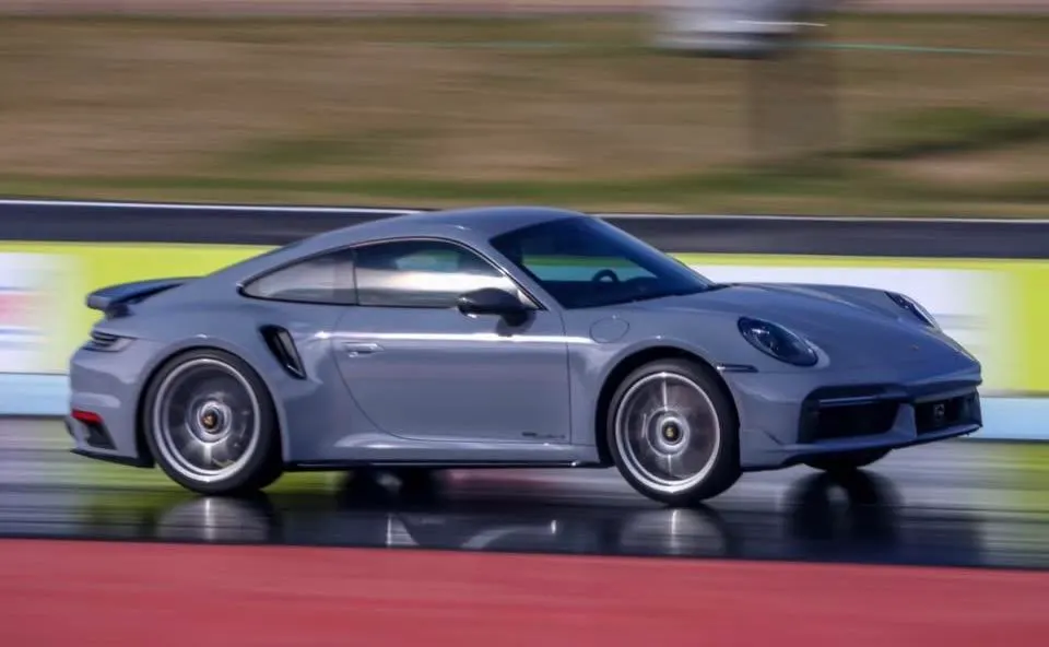 Grey Porsche 911 Turbo S speeding down a drag strip with motion blur, showcasing its sleek design and performance.