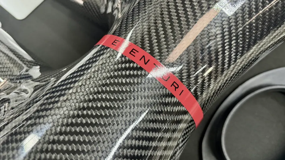 Close-up of an Eventuri carbon fiber intake pipe, showcasing the weave and red branding.