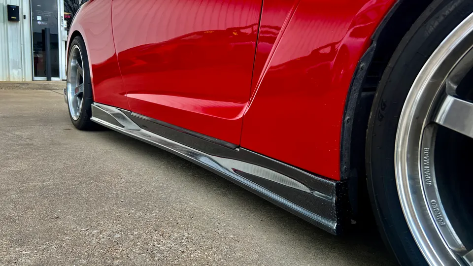 A close-up detail shot of the side of a red car, showcasing a carbon fiber side skirt and custom forged wheels.