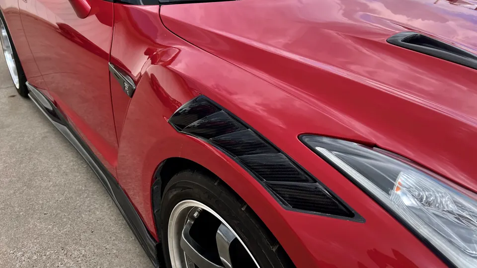 Close-up of a red Nissan GT-R's front fender, showcasing carbon fiber fender vents and side skirt.