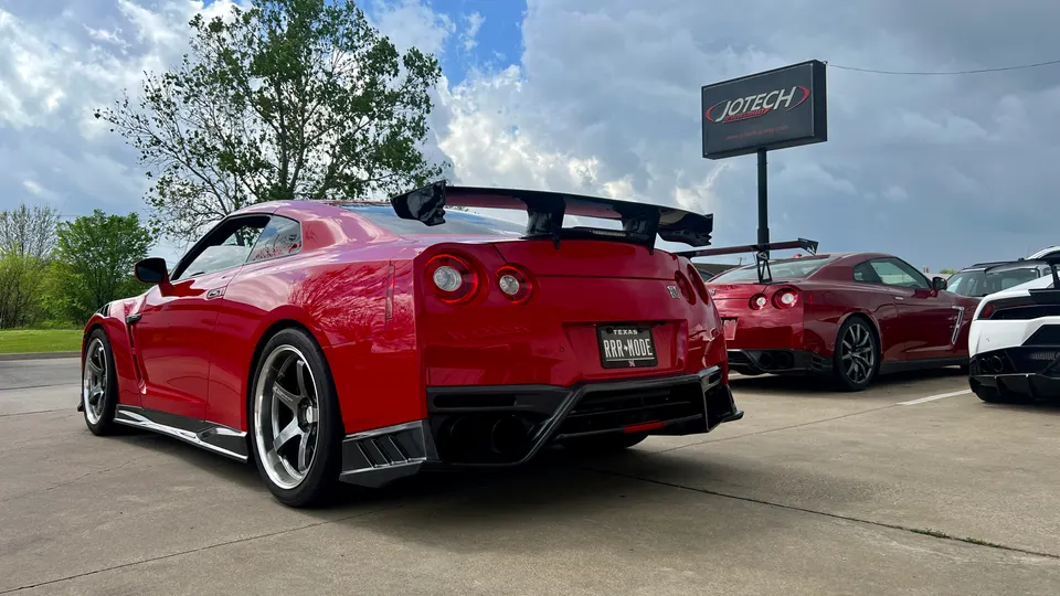Red Nissan GT-R with aftermarket aero and wheels parked outside Jotech Motorsports shop with other performance cars.