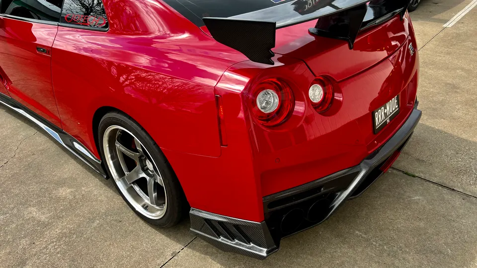 A red Nissan GT-R with a large carbon fiber wing, carbon fiber rear diffuser, and aftermarket wheels parked on concrete.
