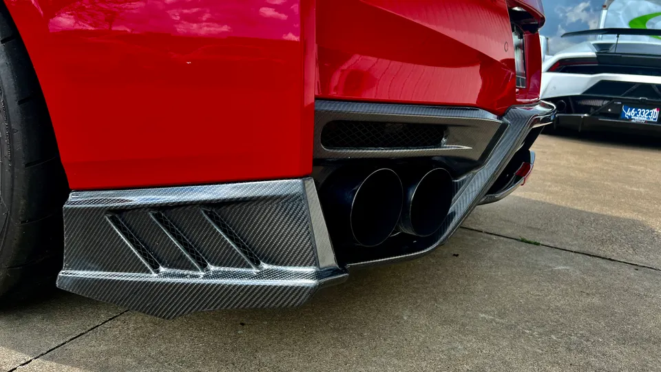 Close-up of a red sports car's rear with a carbon fiber diffuser and dual exhaust tips, parked next to a white Lamborghini.