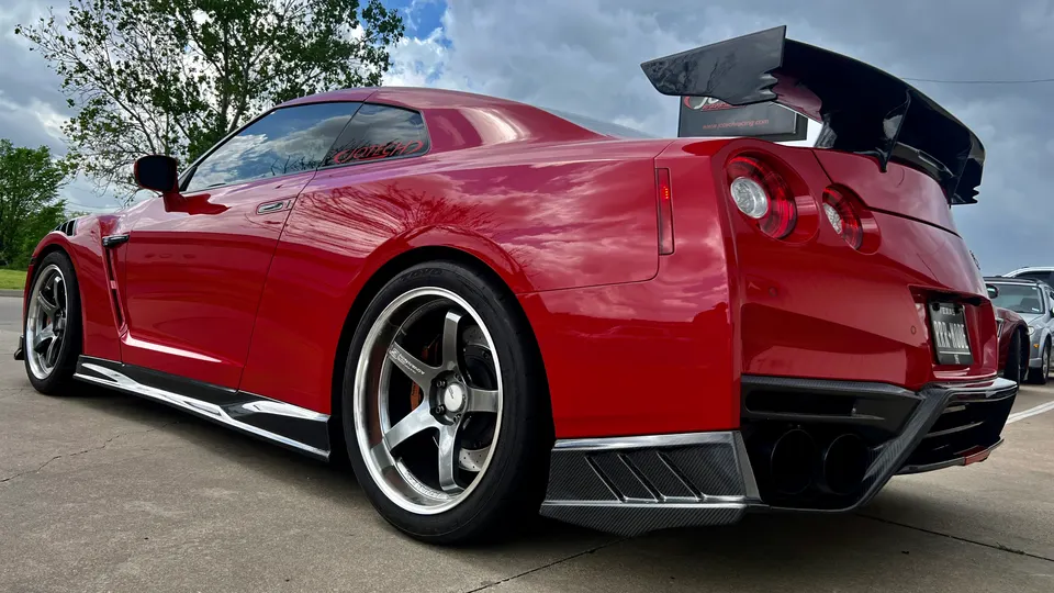 A red Nissan GT-R with a large carbon fiber wing, aftermarket wheels, and a custom rear diffuser parked outdoors.