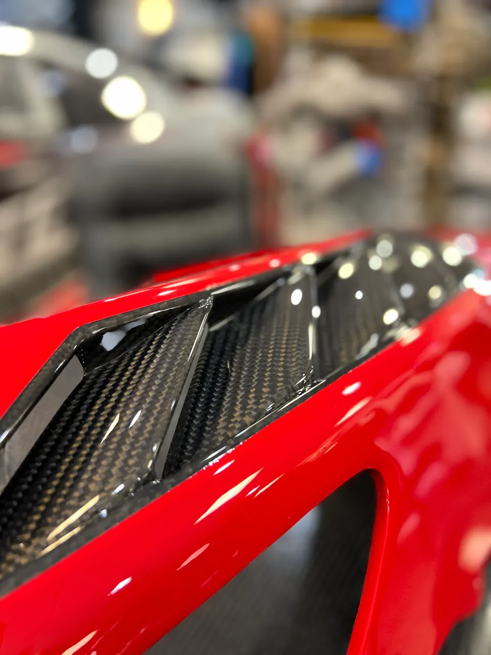 Close-up detail of a red supercar's carbon fiber body panel with vents, showcasing the intricate weave.