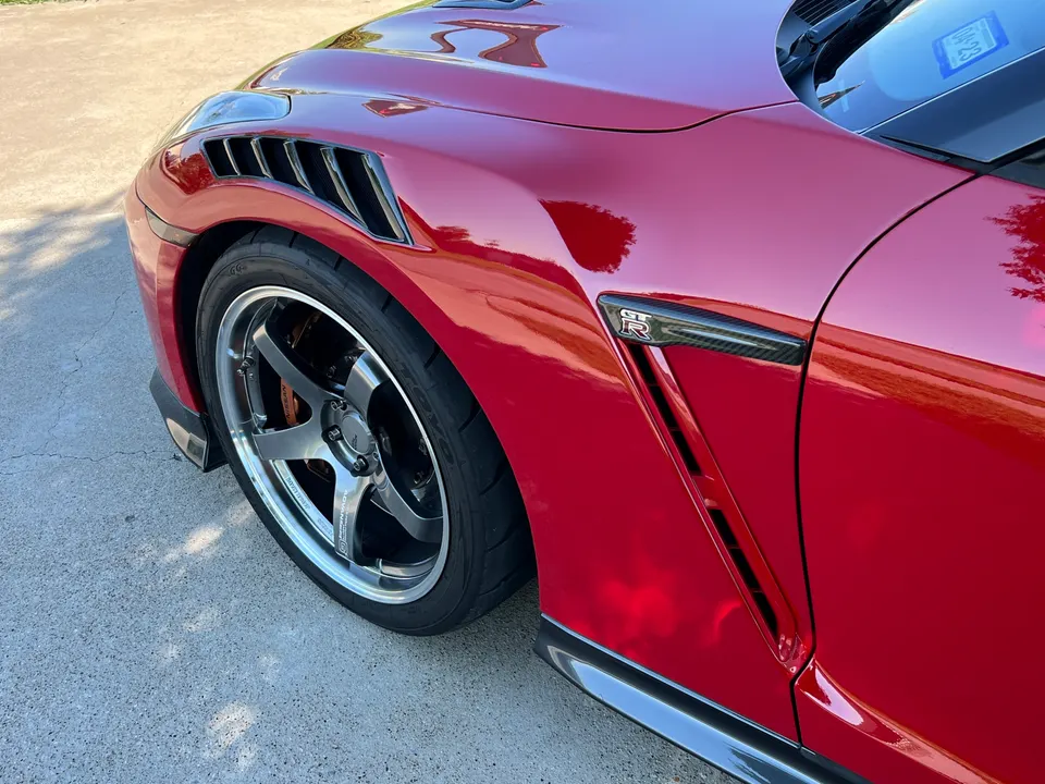 Close-up of a red Nissan GT-R showcasing aftermarket Advan wheels, carbon fiber fender vents, and side skirts.