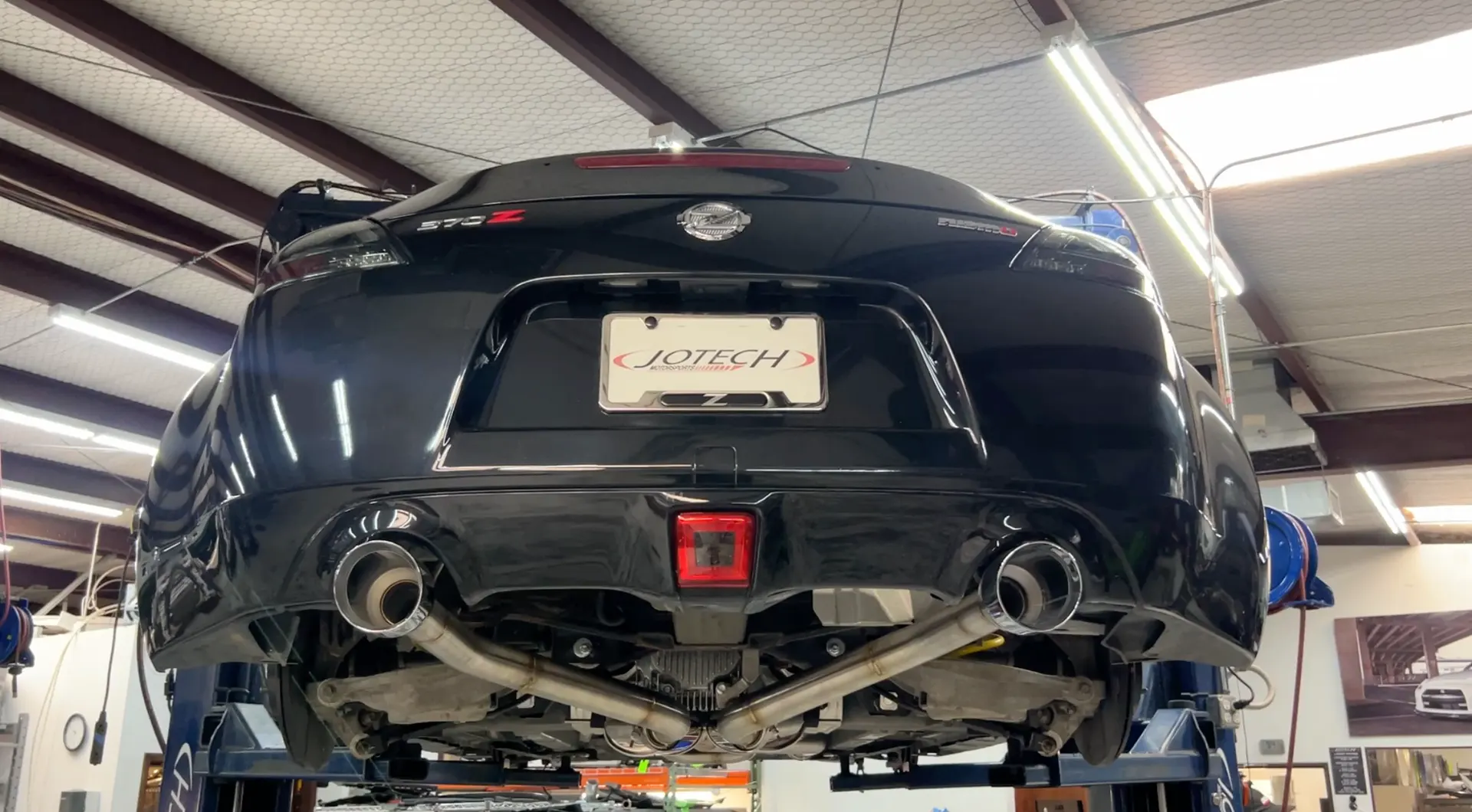 A black Nissan 370Z on a lift in a Jotech Motorsports shop, showcasing an aftermarket exhaust system.
