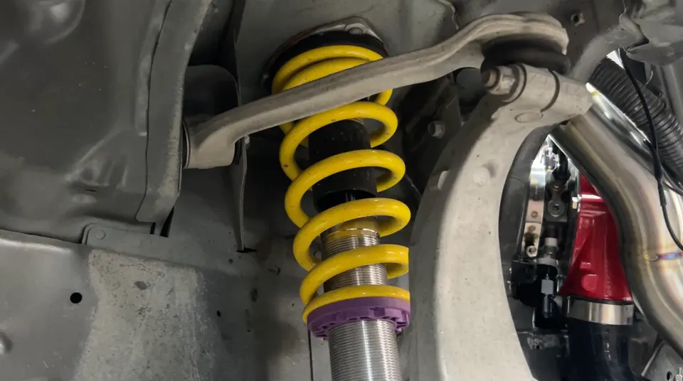 A close-up view of a yellow KW coilover suspension system installed in a car's wheel well.