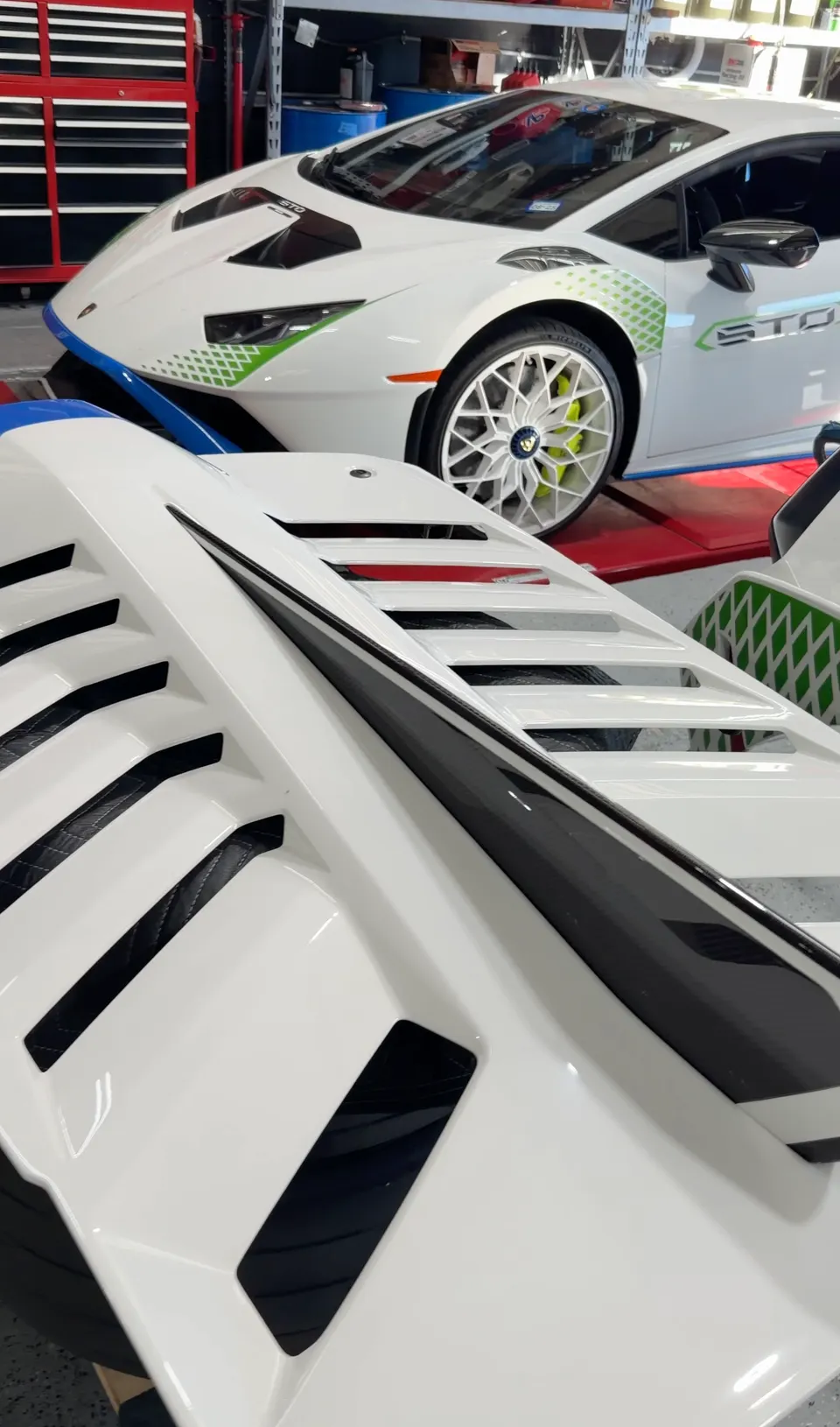 A white Lamborghini Huracan STO in a performance shop with a white vented body panel in the foreground.