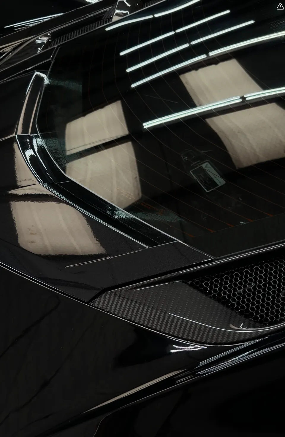 Close-up of a black supercar's rear window and carbon fiber bodywork, showcasing the sleek design and honeycomb grille.