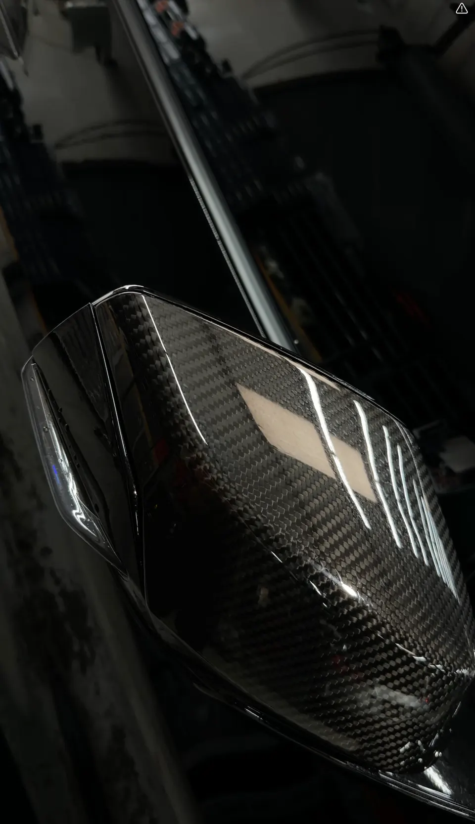 Close-up of a carbon fiber side mirror on a performance car, showcasing the weave pattern.
