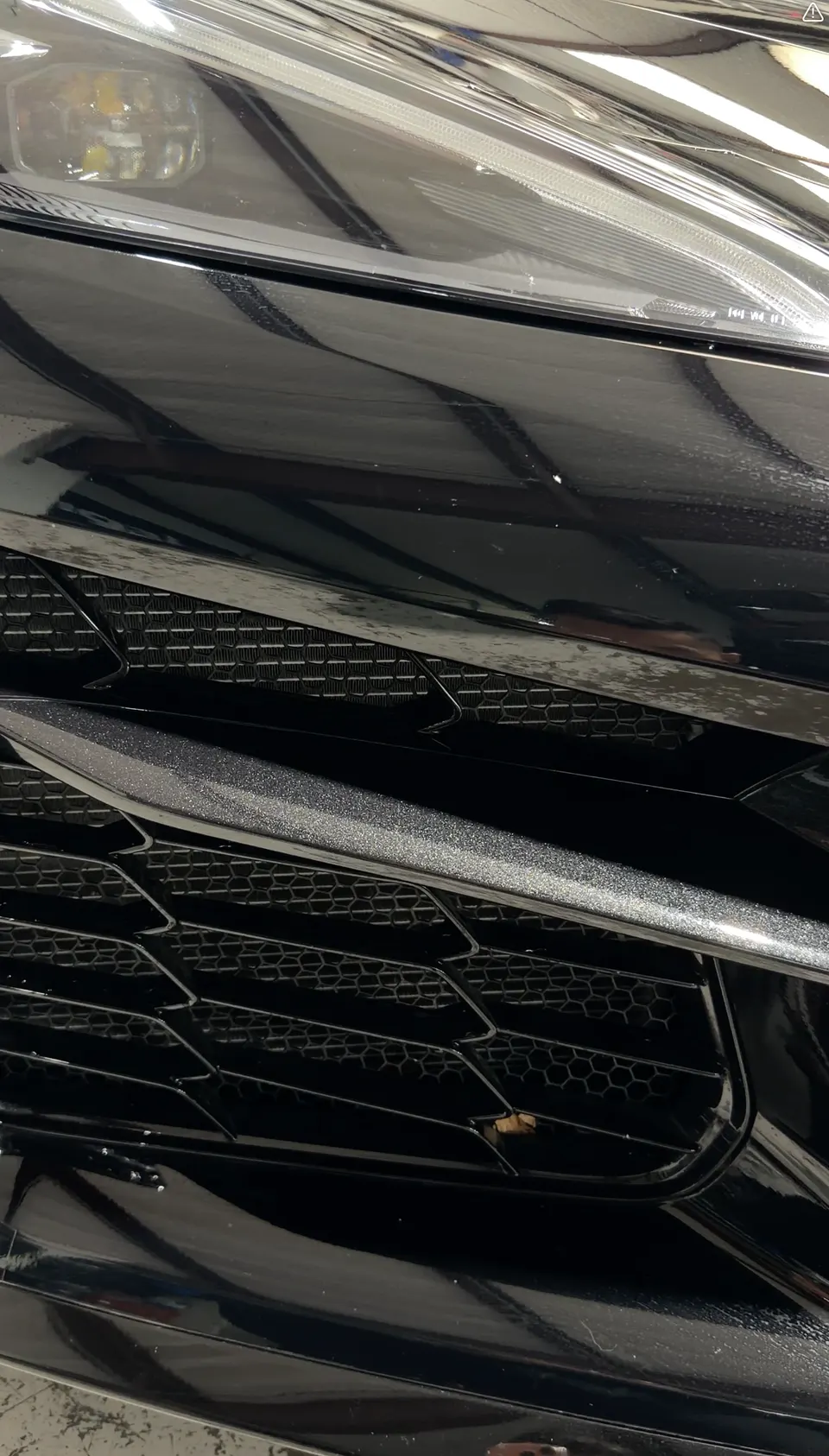 A close-up detail shot of the black car's front bumper, honeycomb grille, and headlight.