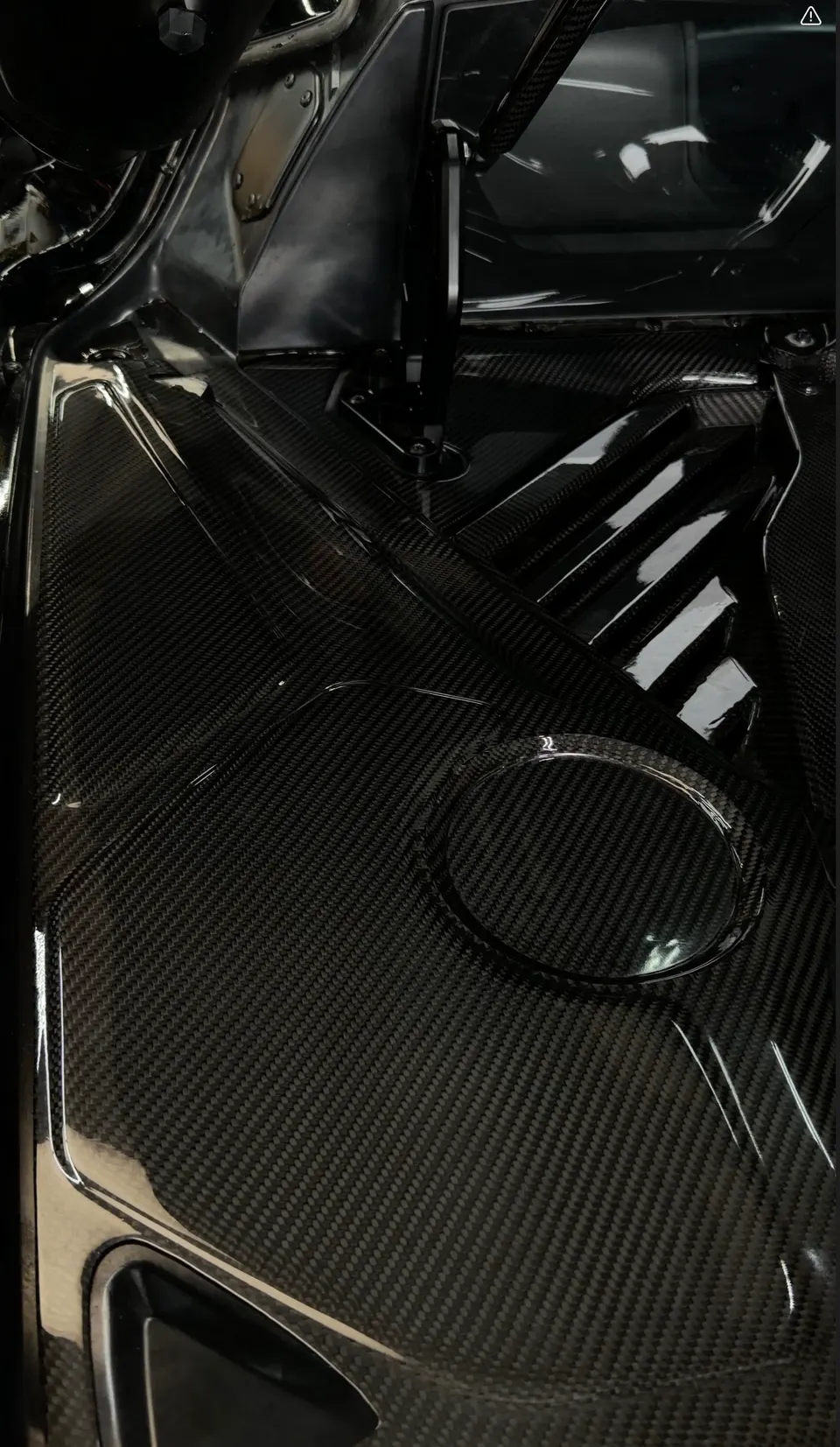 Close-up of a glossy carbon fiber panel in a performance car's engine bay, showcasing the weave.