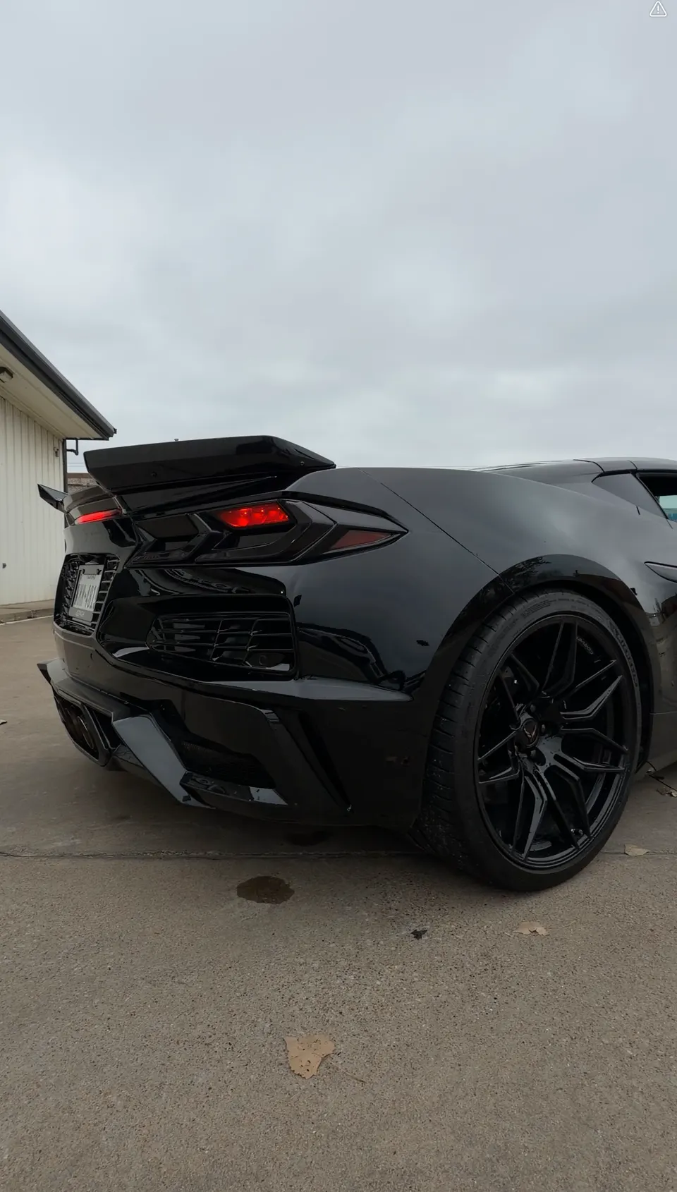 Rear view of a black C8 Corvette with an aftermarket rear wing, diffuser, and black multi-spoke wheels.