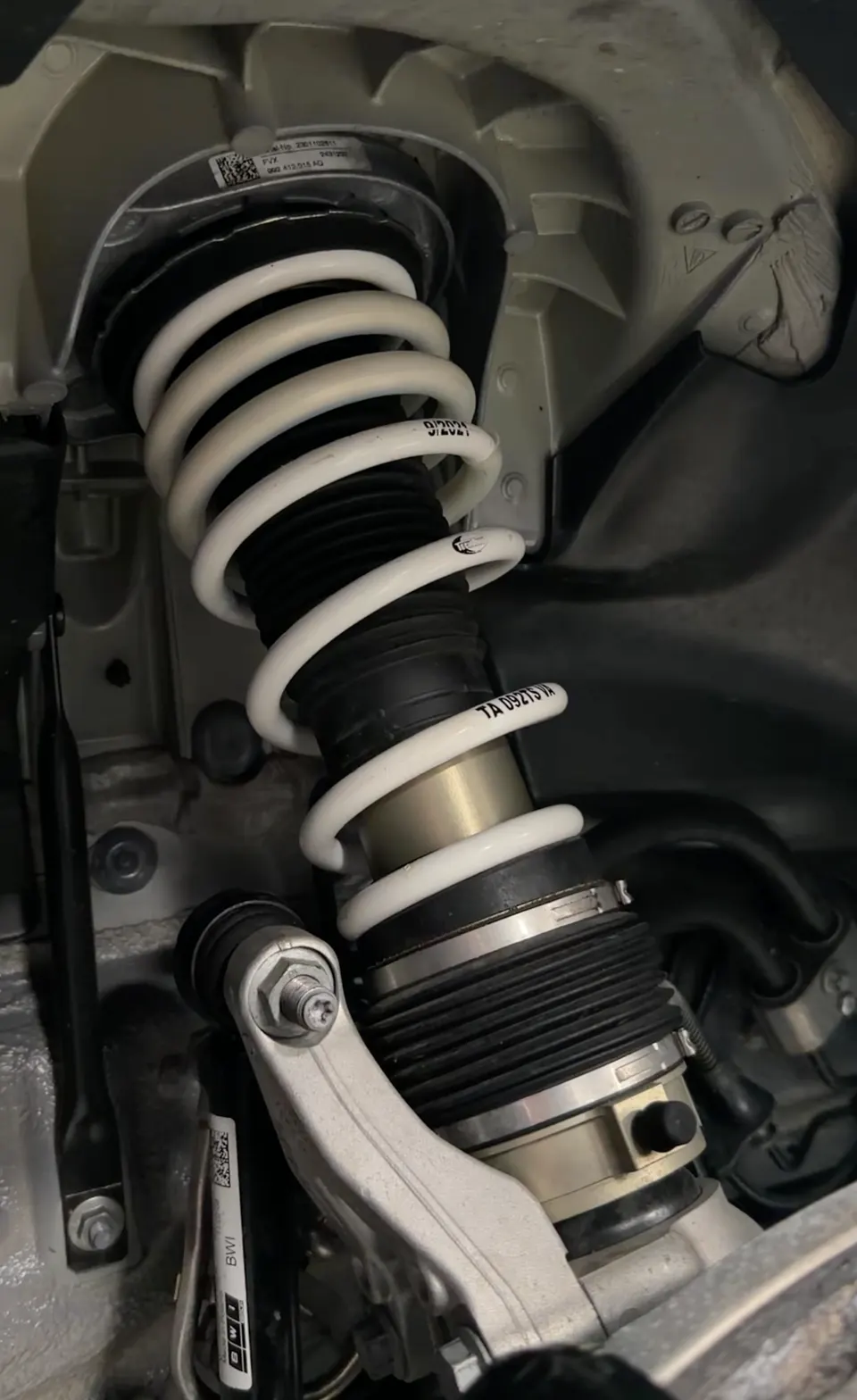 A close-up view of a white coilover suspension system installed in a car's wheel well.