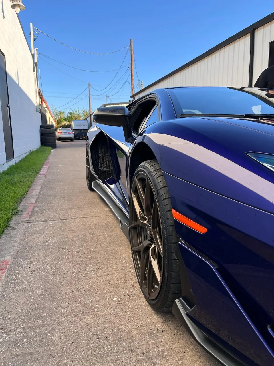 Blue Lamborghini Aventador with custom bronze wheels and side skirts parked in an alley.