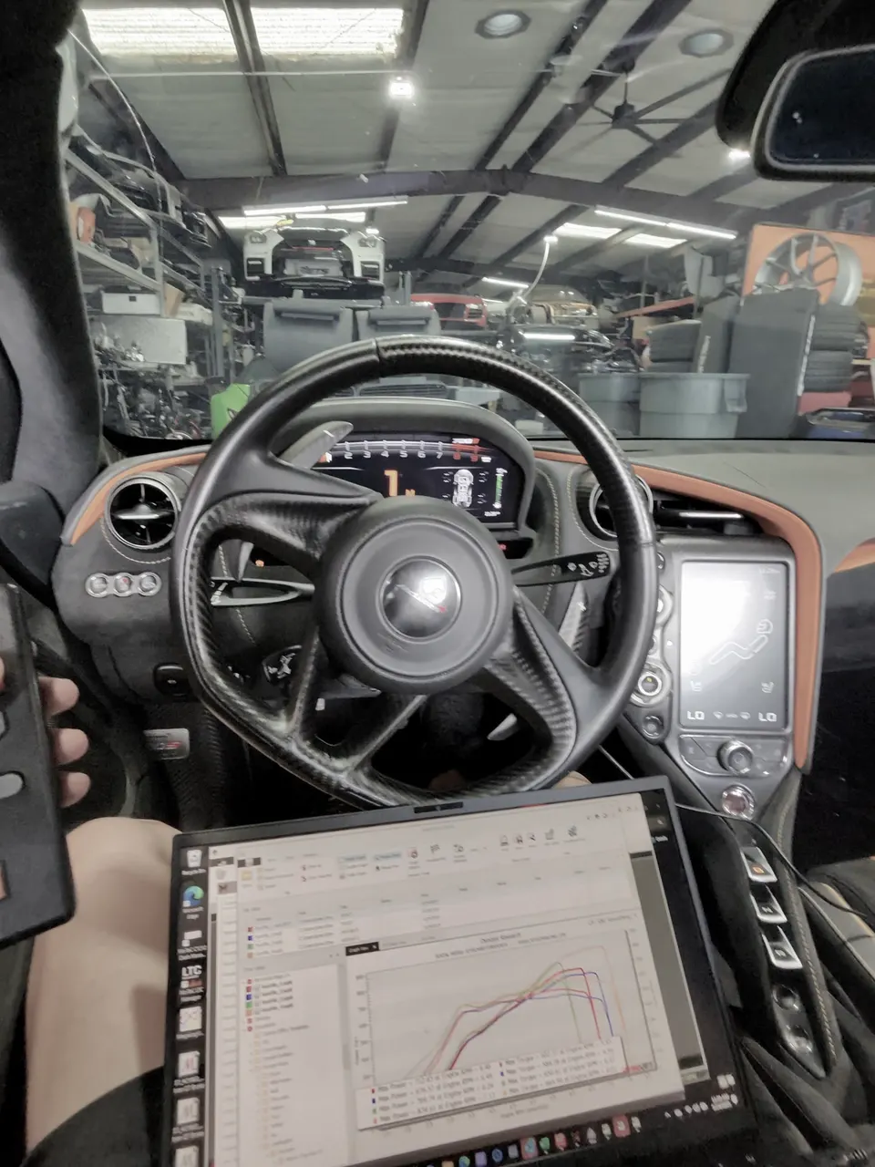 Inside a McLaren, a laptop displays dyno tuning results while the car is in a performance shop.