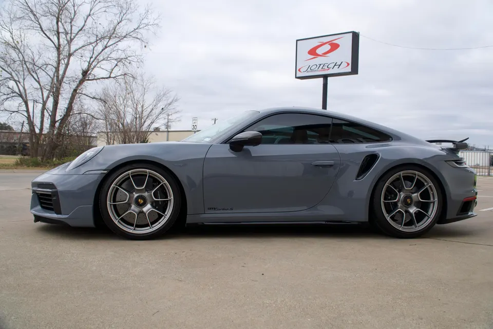 Grey Porsche 911 Turbo S parked outside Jotech Motorsports, showcasing its sleek side profile and custom wheels.
