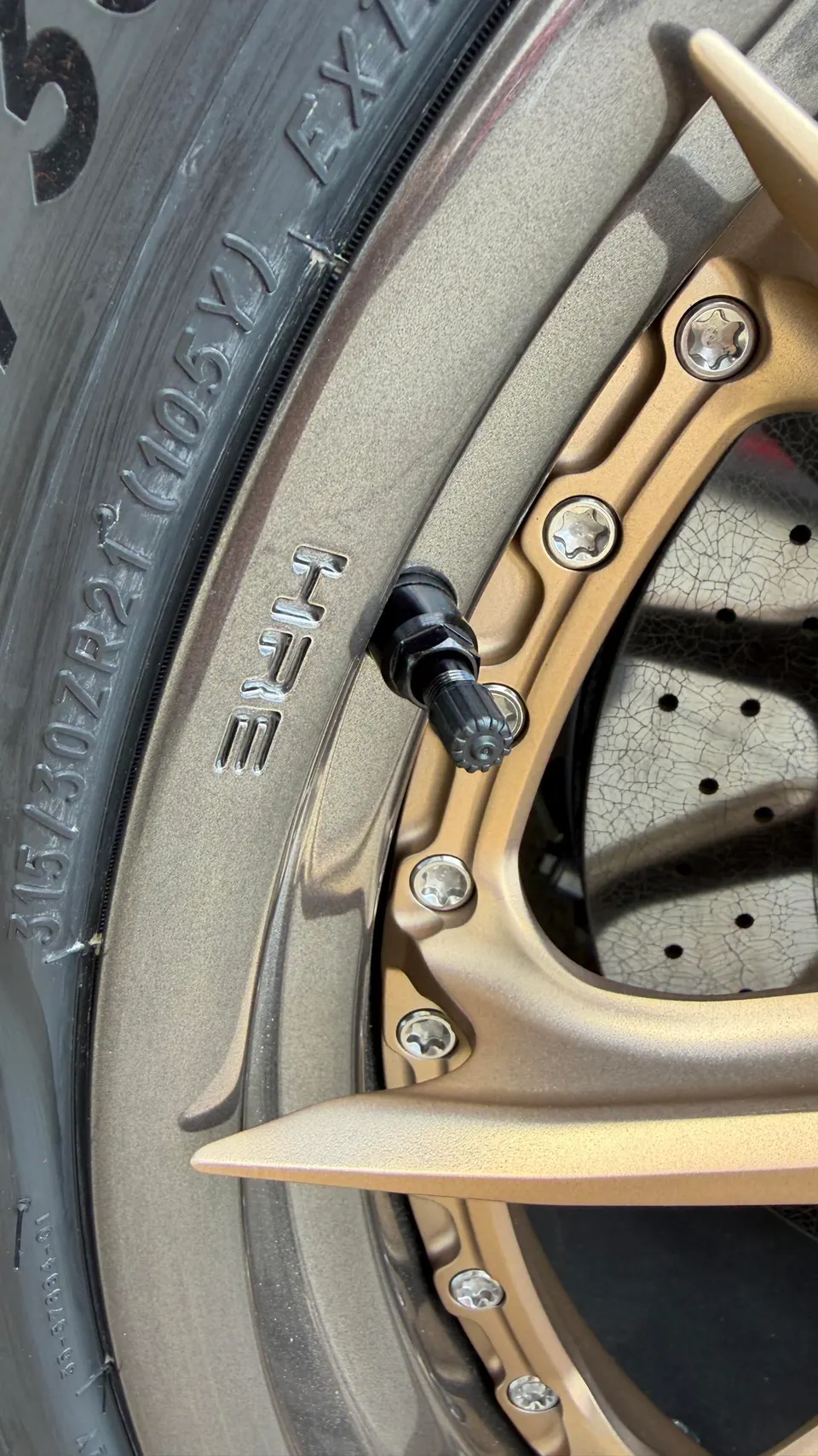 Close-up of a bronze HRE wheel with a tire and a drilled brake rotor, showcasing the valve stem and wheel bolts.