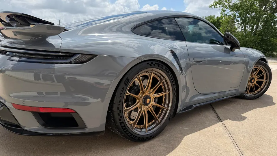 Grey Porsche 911 GT3 RS with bronze aftermarket wheels and a large rear wing parked outdoors.