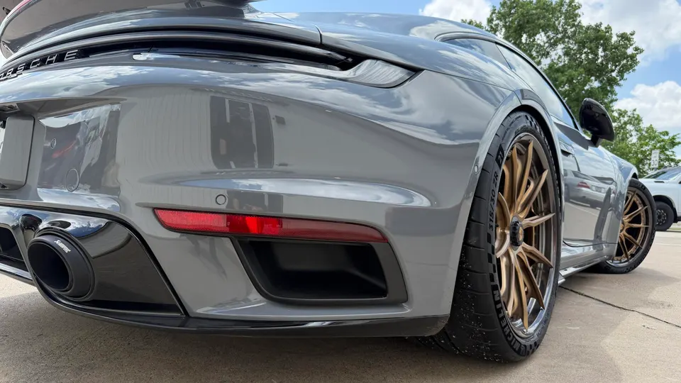 Grey Porsche 911 with Akrapovic exhaust and bronze aftermarket wheels parked outdoors.