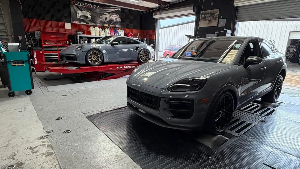 Two grey Porsche cars, a 911 on a lift and a Cayenne on a dyno, inside a performance tuning shop.