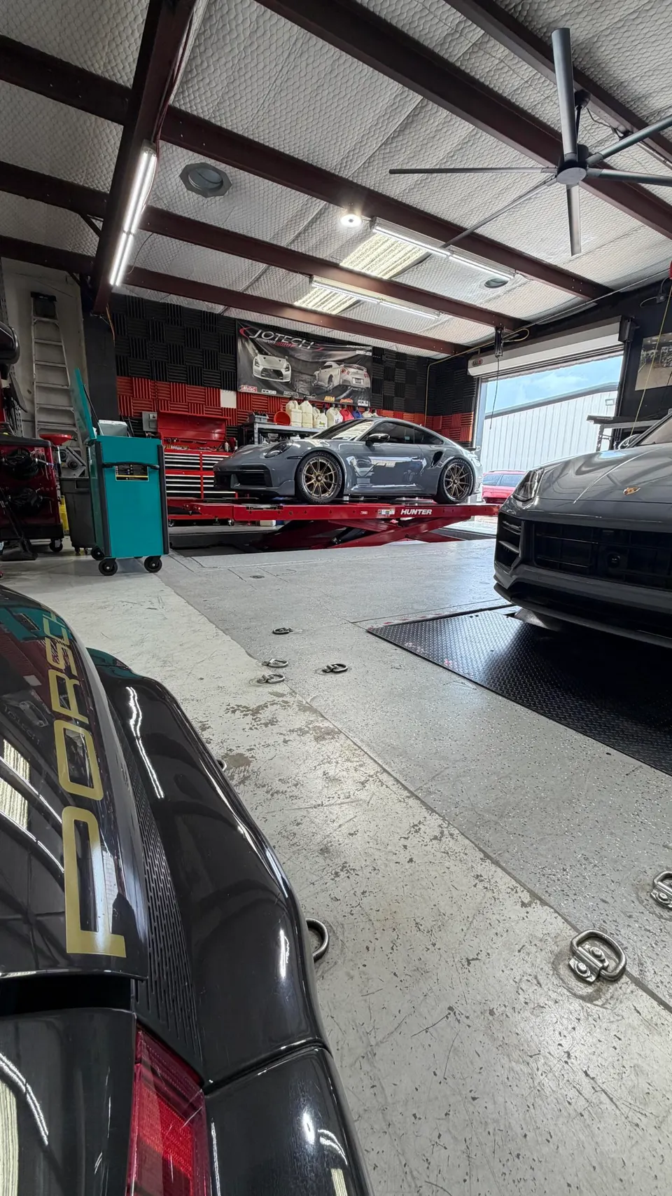 A grey Porsche 911 Turbo S on a red lift inside the Jotech Motorsports tuning shop, with other Porsches visible.