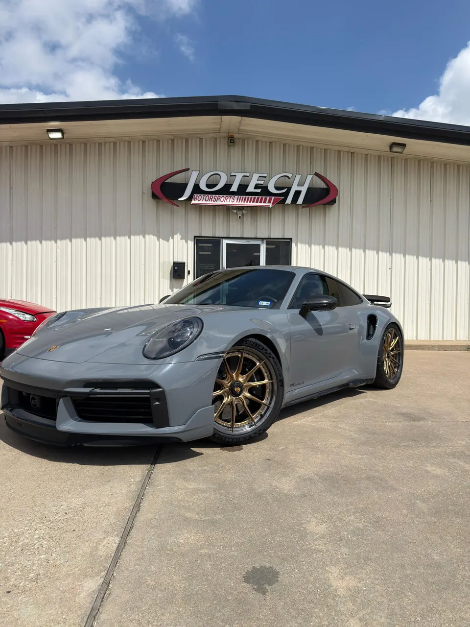 Grey Porsche 911 Turbo S with bronze aftermarket wheels parked in front of Jotech Motorsports shop.