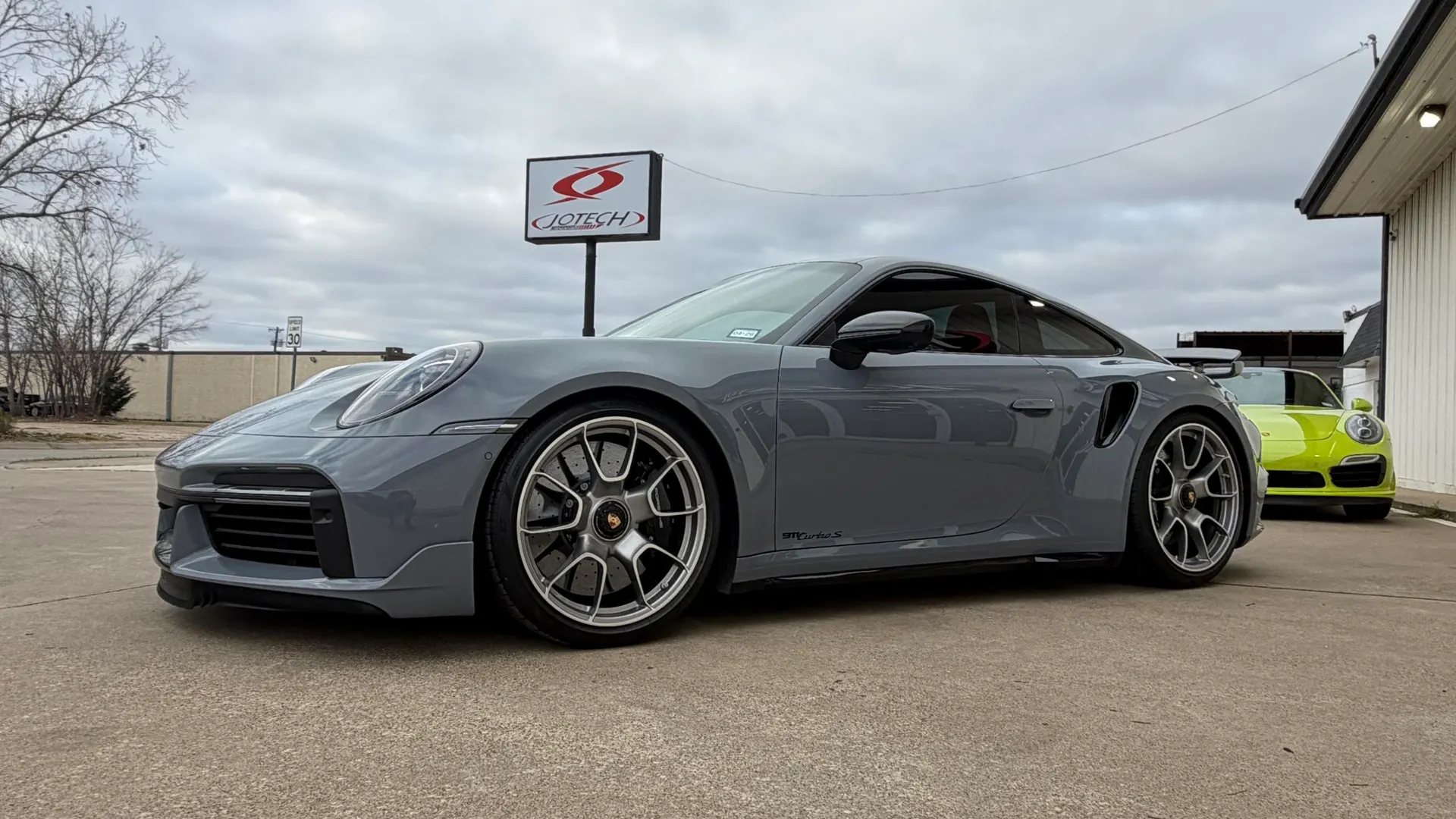Grey Porsche 911 Turbo S parked outside Jotech Motorsports, with a lime green Porsche in the background.