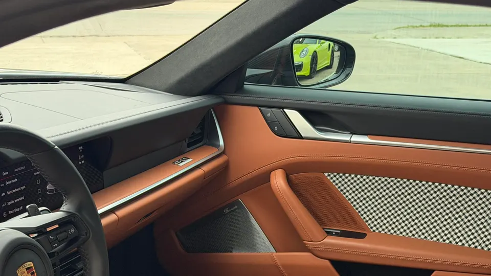 Porsche interior with brown leather and houndstooth door panel, reflecting a yellow Porsche in the side mirror.