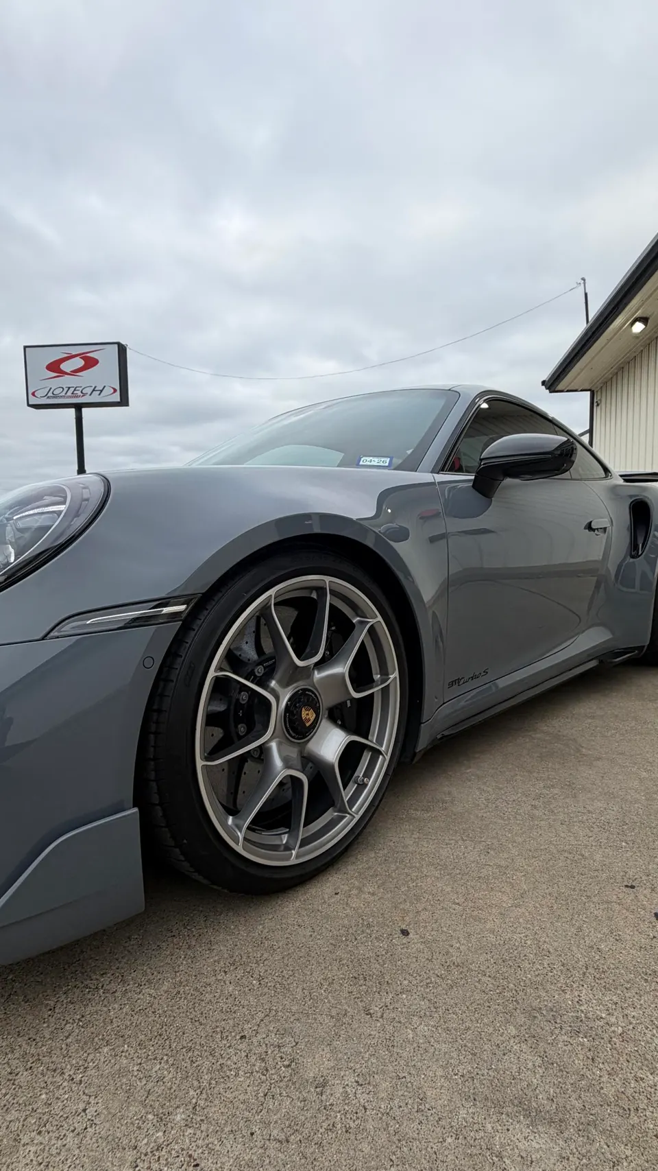 A grey Porsche 911 Turbo S with custom multi-spoke wheels parked outside Jotech Motorsports.