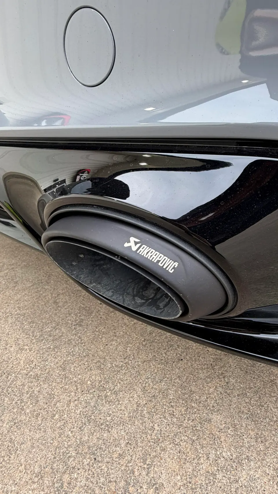 A close-up of a black Akrapovic exhaust tip on a car's rear bumper.