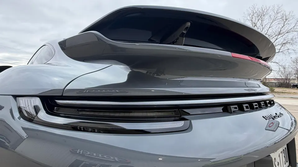 Rear view of a grey Porsche 911 Turbo S with its active rear wing deployed, showcasing the taillights and badging.
