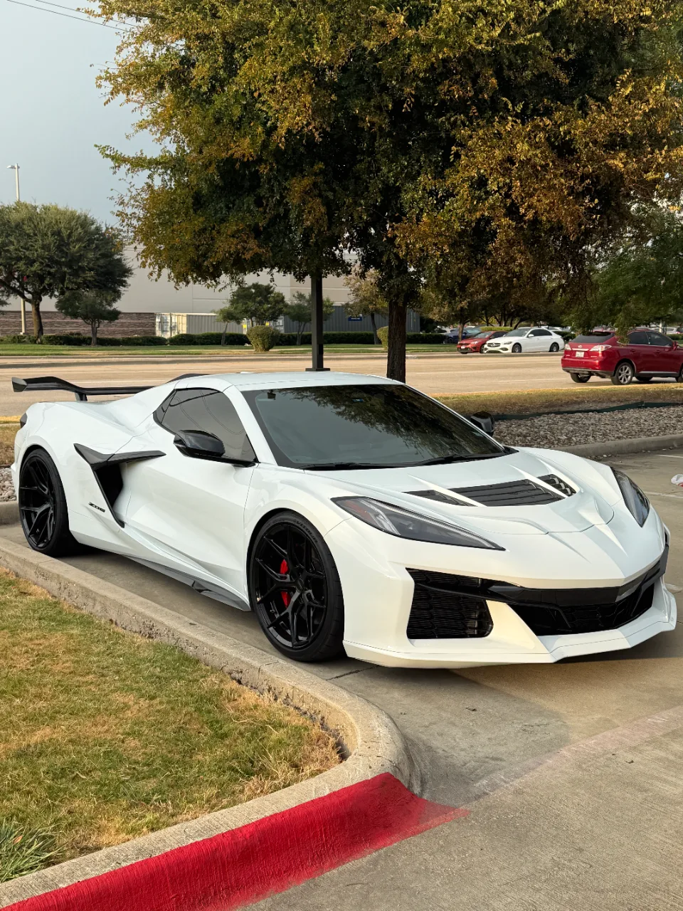 White Chevrolet Corvette C8 Z06 with black wheels and a large rear wing parked on a curb.