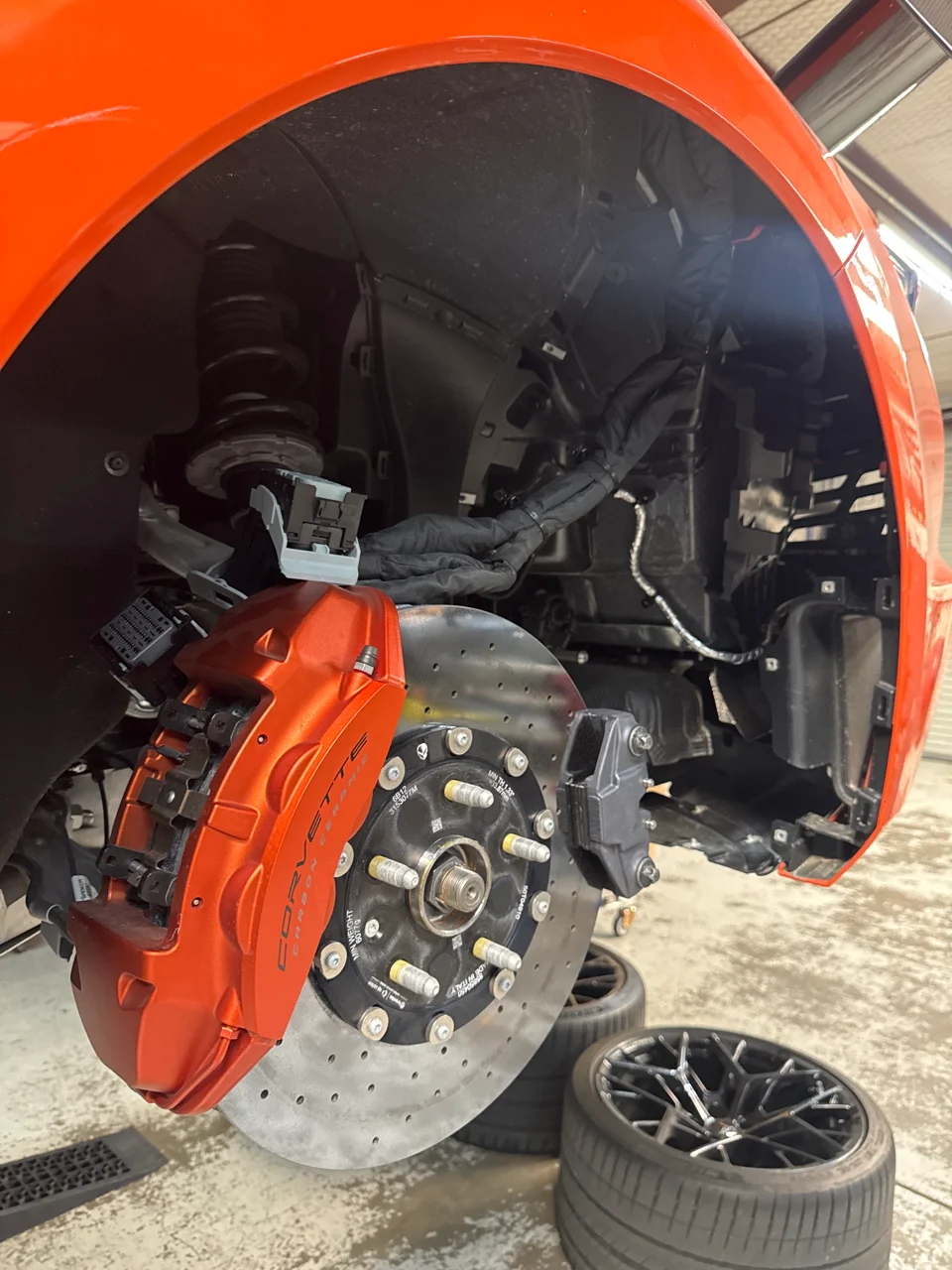 Your Corvette's wheel is off, showing the orange carbon ceramic brakes and suspension components.