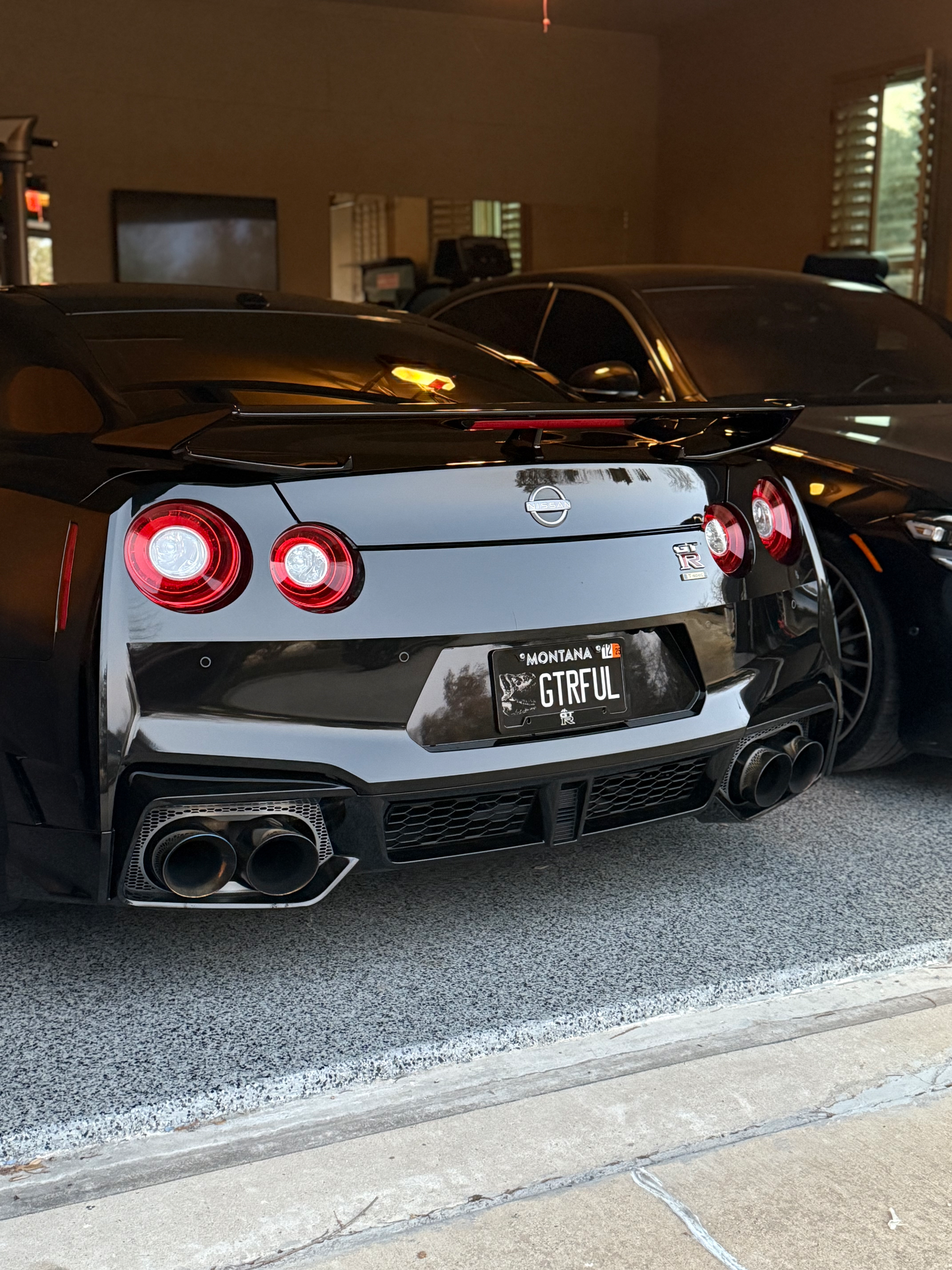 Rear view of a black Nissan GT-R with a custom license plate and aftermarket exhaust tips parked in a garage.