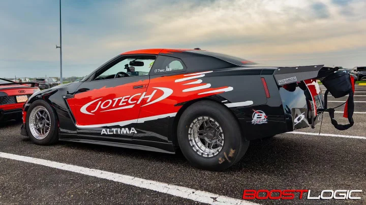 A black and red Jotech Motorsports Nissan GT-R drag car with widebody and parachute on a drag strip.