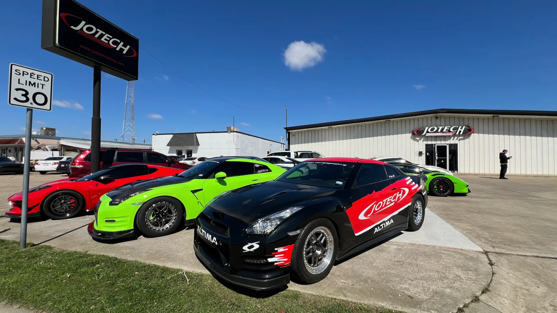 Jotech Motorsports shop exterior with multiple high-performance cars, including Nissan GT-Rs and a Lamborghini, parked outside.