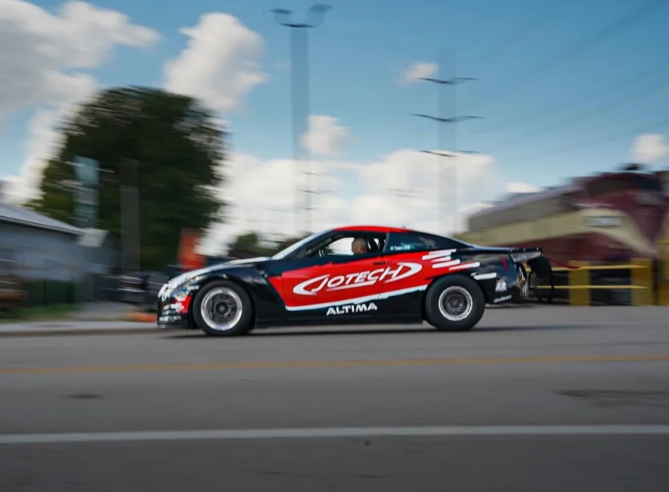A black and red Jotech Nissan Altima drag car in motion, featuring custom livery and drag racing wheels.