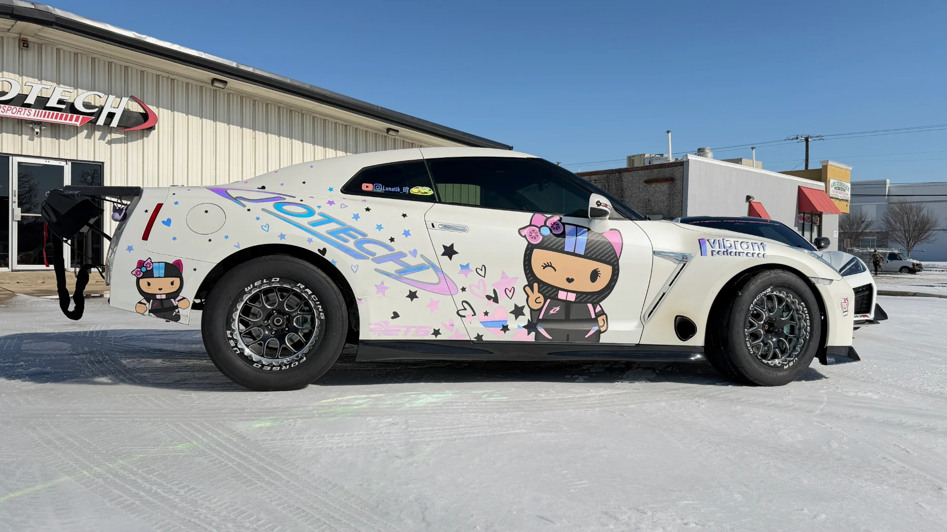 A white Nissan GT-R drag car with a custom Hello Kitty-themed wrap and Weld Racing wheels parked outside Jotech Motorsports.